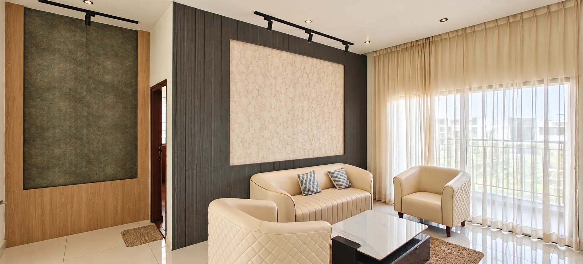 Contemporary living room with a cream sofa and quilted armchairs, textured wall panels, a white coffee table and sheer curtains at a model apartment in Whitefield, Bangalore